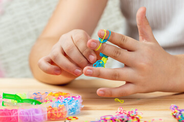 Hands of a girl weaving a bracelet with multi-colored rubber bands. Development of fine motor skills of fingers