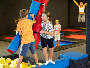 Children having funny wrestling by inflatable logs with his friends in indoor amusement playground