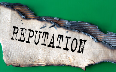 REPUTATION - word on green paper against the background of a sheet of paper damaged by fire