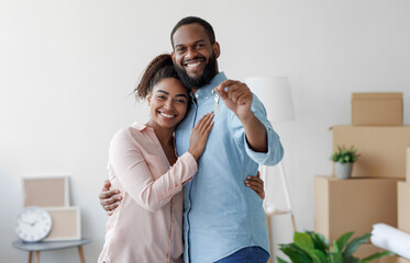 Happy smiling young african american loving family hugging in new home among boxes and showing...