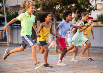 Group of happy multiracial kids running through city streets during summer day.