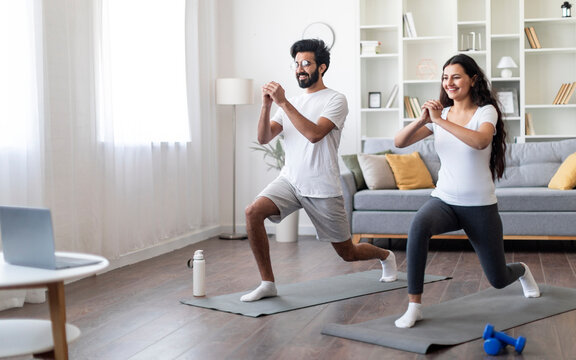 Training At Home. Sporty indian couple doing glutes exercise in front of laptop, happy young eastern spouses watching online tutorials and exercising in living room, practicing sports together