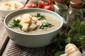 Delicious mushroom cream soup with croutons, parsley and ingredients on wooden table, closeup