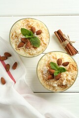 Delicious rice pudding with cinnamon, almonds and mint on white wooden table, flat lay