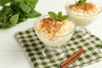 Delicious rice pudding with cinnamon and mint in glass dessert bowls on white wooden table, closeup