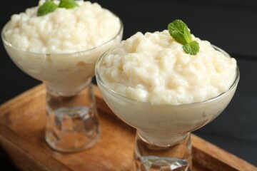 Delicious rice pudding with mint in glass dessert bowls on black table, closeup