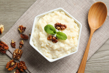 Delicious rice pudding with walnuts, mint and spoon on wooden table, flat lay