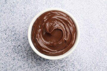 Delicious chocolate pudding in bowl on light grey textured table, top view