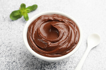 Delicious chocolate pudding in bowl and spoon on light grey textured table, closeup