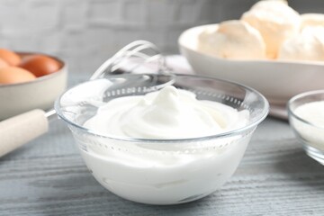 Whipped cream in bowl and other ingredients on gray wooden table, closeup. Cooking meringue cookies