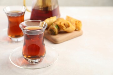 Traditional Turkish tea in glass cups, teapot and fresh baklava on white table, closeup. Space for text