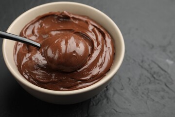 Taking tasty chocolate pudding from bowl with spoon on black table, closeup