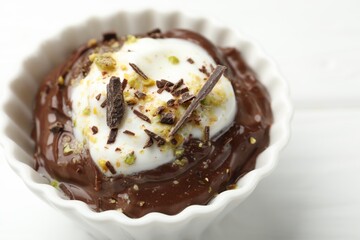 Tasty chocolate pudding with whipped cream in bowl on white wooden table, closeup