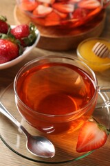 Aromatic fruit tea with strawberries and honey on wooden table, closeup