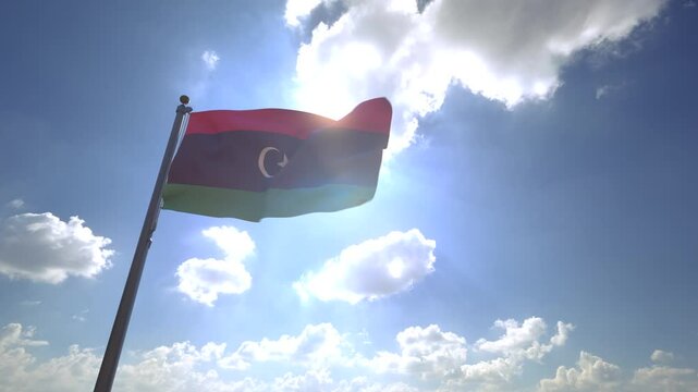 Libya Flag waving on a Flagpole from a Moving Angle in front of a blue sky with clouds	