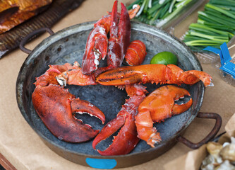 Fresh grilled lobcter claws at grill pan. Seafood delicacy barbecue outdoors. Picnic healthy food, lobster pieces in shells cooked at large metallic pan with lime. Mediterranean cuisine