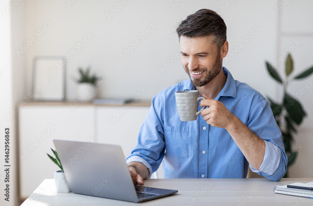 Poster handsome smiling businessman drinking coffee and using laptop in office, checking emails on computer