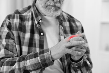 Arthritis. Senior man suffering from pain in finger indoors, closeup. Black and white toning with...