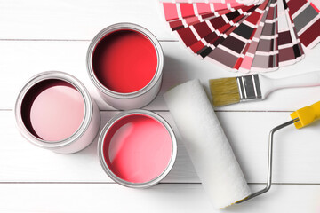 Cans with paint in shades of red, color palette, roller and brush on white wooden background, top...