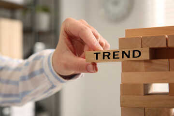 Woman removing wooden block with word Trend from tower indoors, closeup