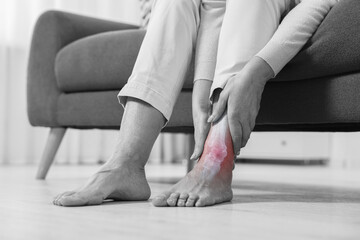 Arthritis. Woman suffering from pain in leg at home, closeup. Black and white toning with red color...