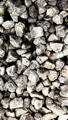 Various sizes of gray stones are scattered on a surface in natural light at a landscaping site