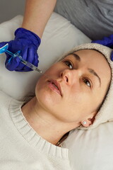 Close-up of a young woman receiving a cosmetic injection from a medical professional wearing gloves. The woman is lying on a treatment table