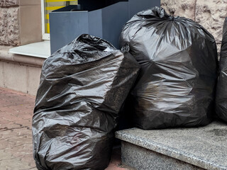 Two large black garbage bags rest against a stone ledge near a building, showcasing urban waste disposal habits