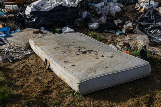 Mattresses clutter a trash-filled space, highlighting urban neglect and waste issues in an environment affected by litter