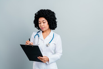 Female doctor in medical uniform taking notes on clipboard during consultation in a healthcare clinic environment