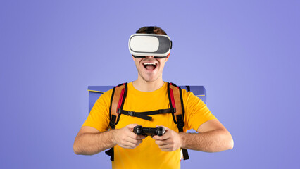 Virtual tourism. Excited millennial guy with VR headset and controller watching travel tour in cyberspace over blue studio background. Happy young man having vacation or journey in augmented reality