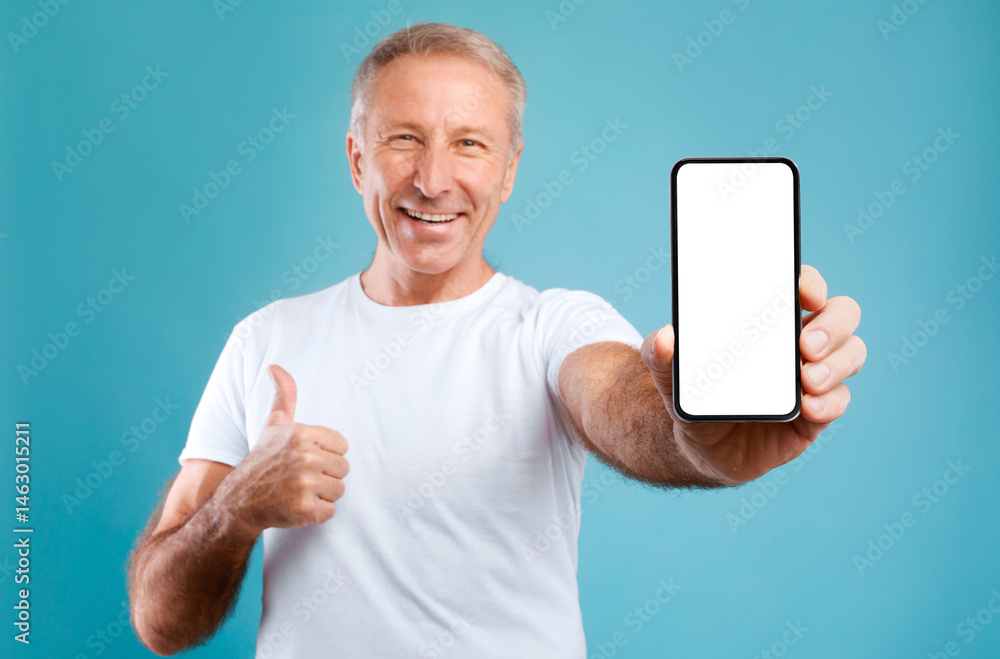 Poster I Recommend. Portrait of smiling mature man holding smartphone with white blank screen in hand showing device and thumb up gesture. Selective focus on gadget with empty free space for mock up template