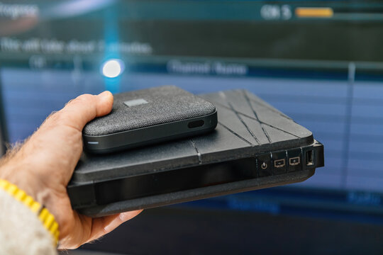 Paris, France - Feb 17, 2025: A hand holds two Orange Livebox internet TV routers, with an older generation box at the bottom featuring buttons and ports, and a compact newer model 