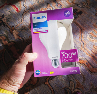 Paris, France - Feb 7, 2025: A hand holds a Philips LED light bulb box labeled Cool White 4000K with 23W power and 3452 lumens output, shown on a decorative carpet in bright indoor light