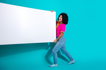 Smiling young woman holding a white signboard against a vibrant teal background wearing colorful...