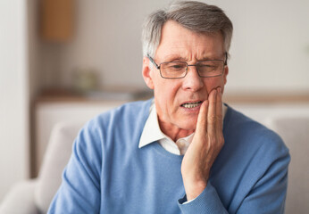 Elderly Man Having Toothache Touching Cheek Suffering From Pain Sitting On Sofa At Home. Selective...
