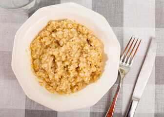 There is portion of freshly prepared milk oatmeal porridge in plate. Traditional dietary European breakfast.