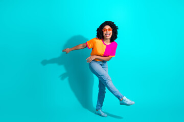 Young woman dancing joyfully against a bright turquoise background wearing colorful fashion inspired by vibrant casual style