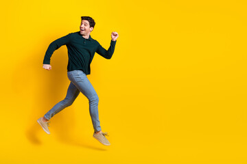 Fototapeta na wymiar Cheerful young man in casual green attire jumping against a vibrant yellow background showing excitement and positivity