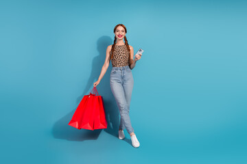 Young stylish woman in casual wear holding shopping bags and smartphone with a cheerful expression...