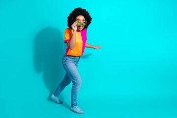 Joyful young woman in vivid casual attire posing energetically against a teal background while...