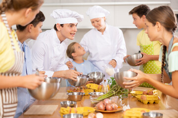 Enthusiastic young chef giving culinary classes to group of interested curious tween girls and...
