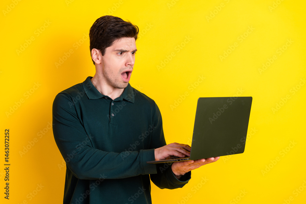 Poster young man with a surprised expression using a laptop computer against a bright yellow background