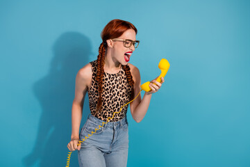 Young woman with braids angrily shouting into a yellow phone against a vibrant blue background,...