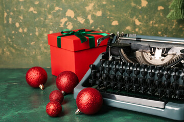 Vintage typewriter with Christmas balls and gift box on green background