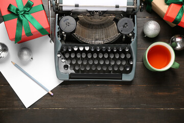 Vintage typewriter with Christmas balls, gift boxes and cup of tea on wooden background