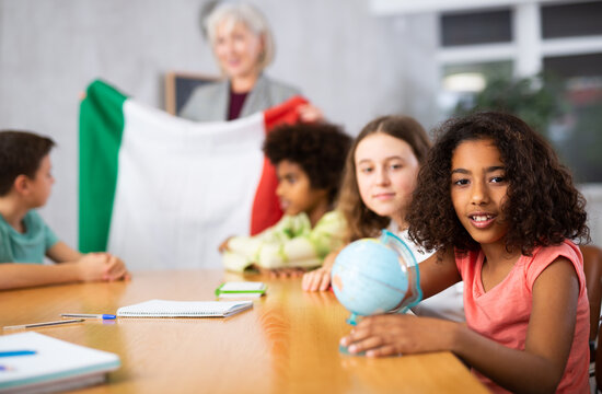 in geography lesson, students carefully listen to woman teacher who talks about Italy