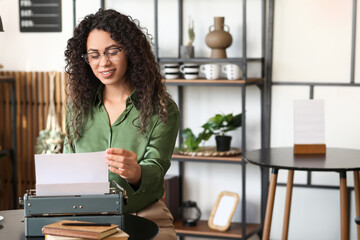 Young African-American author using typewriter at table in cafe