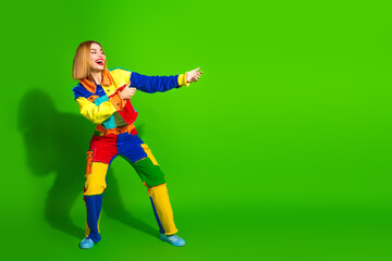 Colorful young woman in trendy patchwork outfit posing happily against a vivid green background with cheerful gestures