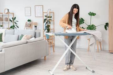 Beautiful young happy woman ironing trousers on board at home